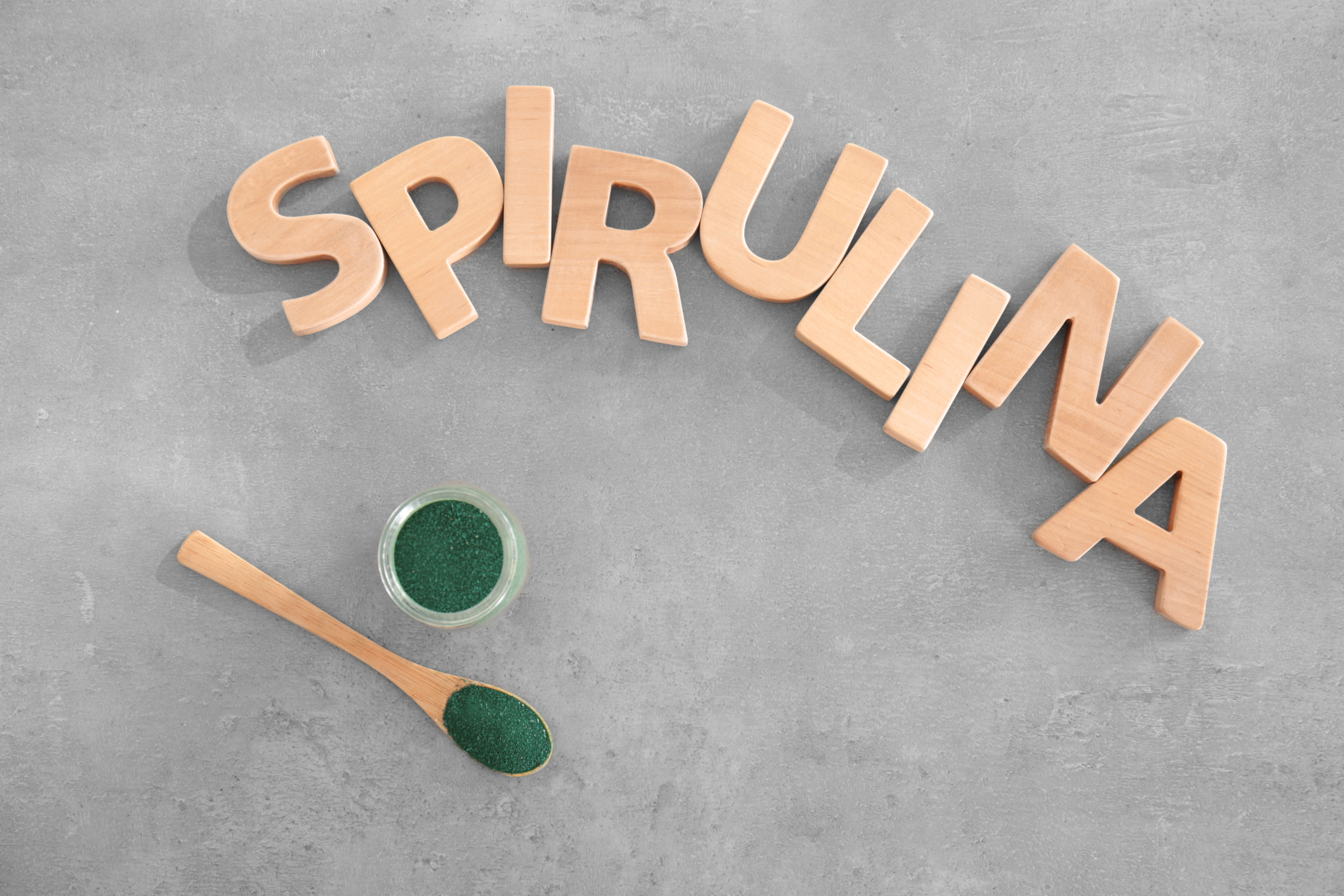 Composition with letters, spoon and jar with spirulina powder on gray background